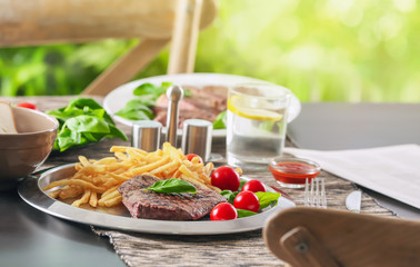 Silver plate with delicious steak and fries on table in restaurant