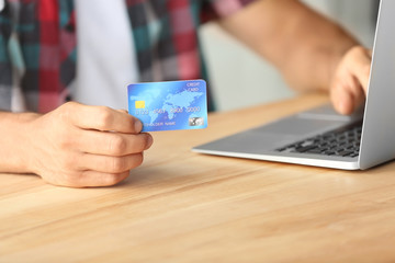 Man holding credit card while using laptop indoors