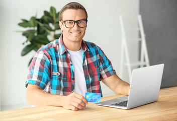 Young man holding credit card while using laptop at home