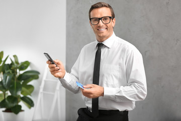 Businessman holding credit card and smartphone indoors