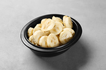 Bowl with yummy sliced bananas on grey background