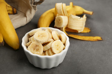 Bowl with banana slices on grey background