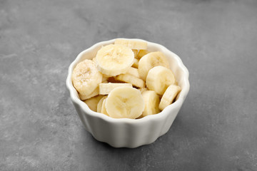 Bowl with yummy sliced bananas on grey background