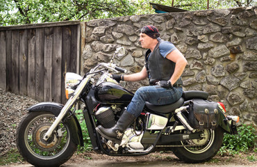 Fototapeta na wymiar The biker sits on a motorcycle in the yard of his house