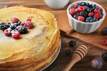 Plate with delicious thin pancakes and berries on wooden background