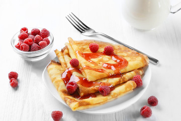 Plate with delicious thin pancakes and berries on wooden background