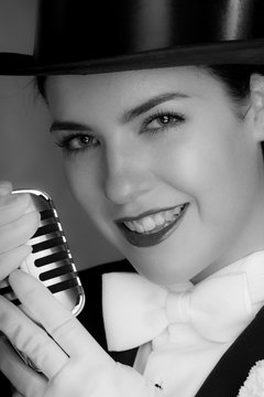 Young woman wearing top hat and singing into microphone.