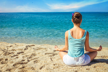 Fototapeta na wymiar Young woman meditates on the beach