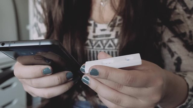 Woman holding a pregnancy test in her hand and texting with the other on her smartphone