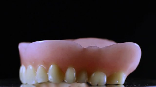Dental jaw prothesis with white full teeth on black background.