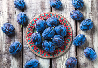 Plums overhead group on colorful plate on old rustic white wooden table in studio
