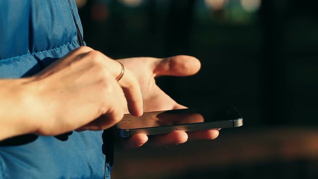 Close-up shot of male hands scrolling and scaling screen on smartphone at city park.