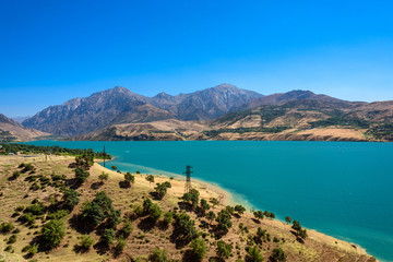 Fototapeta na wymiar Panoramic view of Charvak Lake, artificial lake-reservoir created by erecting a high stone dam on the Chirchiq River, and range of mountains on the background located in Tashkent region of Uzbekistan