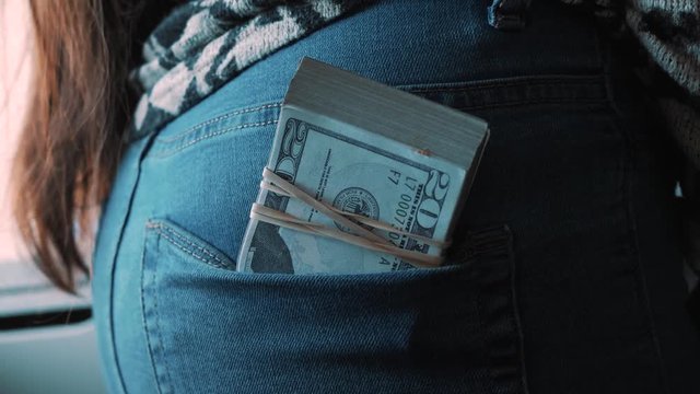 Girl putting a large stack of money bills in the back pocket of her jeans