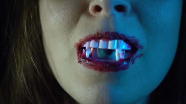 The blue eye moves and peeps through the teeth of a female vampire from the mouth, close-up shoot 4k.