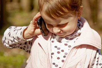 Happy cute little child girl talking phone outdoors. Emotional facial expressions.