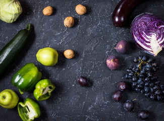 Fresh organic raw green and purple colored vegetables and fruits on dark stone background