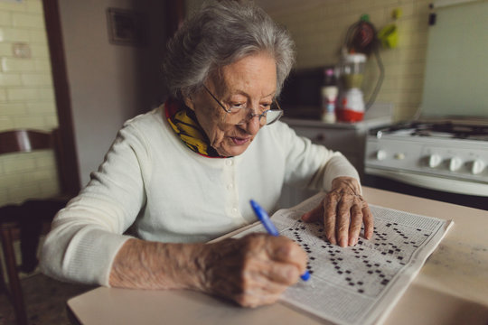 Old woman solving crossword puzzles in the kitchen