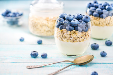 Clear bowl of yogurt with fresh  blueberries and oatmeal  on a turquoise wooden background