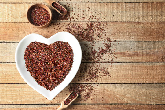 Plate in shape of heart with quinoa seeds on wooden table