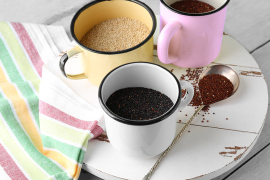Mugs with different quinoa seeds on wooden board