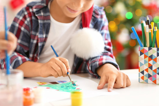 Cute boy painting Christmas fir tree at table