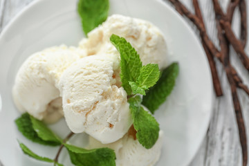 Plate with yummy vanilla ice cream on wooden table, closeup