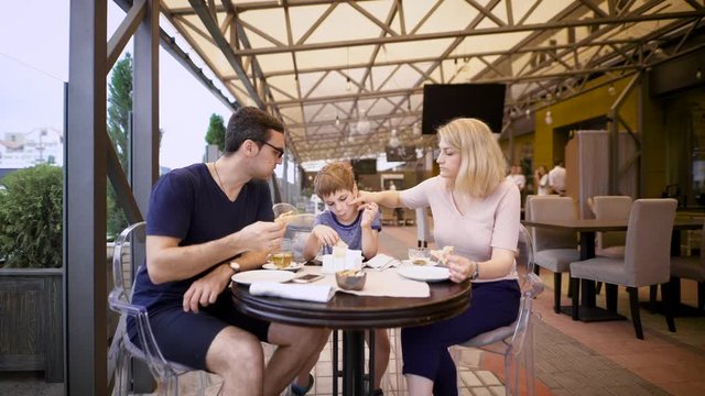 Image of a happy family and their son at the cafe. Loving couple with child are spending time together in pizzeria. Mother, father and son relaxing in restaurant eating pizza and drinking hot tea.