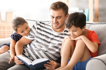 Fototapeta premium Young man and his little children reading book at home