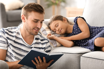 Young man reading book to his little sleeping daughter at home