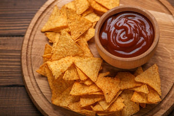 Mexican nachos chips with spicy tomato sauce on wooden background. Flat lay. The concept is harmful food, cafe, pub.