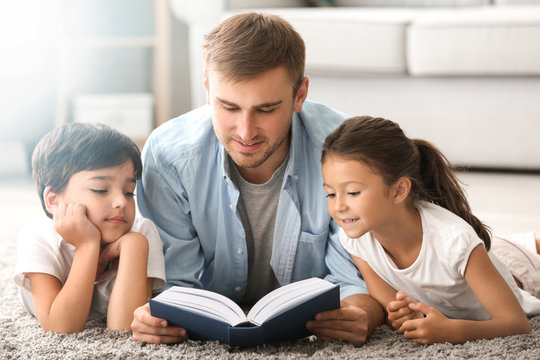 Young man and his little children reading book at home
