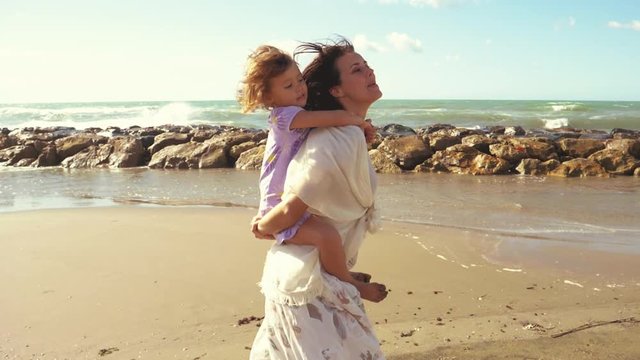 Little girl piggyback on mother singing happy in front of ocean slow motion