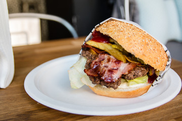 Smaczny Burger wołowy na białym talerzyku owinięty w papierem - bekon i warzywa 