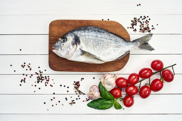 Fresh dorado fish on wooden cutting board with garlic, tomatoes, basil and peppercorns. Top view, copy space