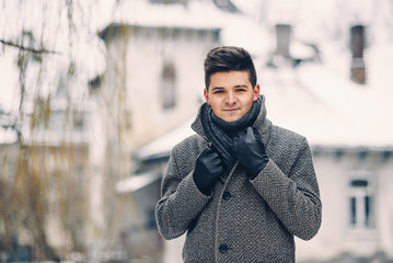 A handsome smiling young man in a warm coat and leather gloves while walking on the city.