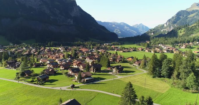 Aerial shot of traditional swiss village in Switzerland on a sunny day. Summer scenery of small town with view of houses on green grassy hills,majestic mountains in background under clear blue sky