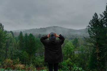 The young happy girl raised her hands up to the sun, against the mountain and sunset sky