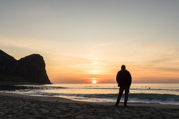 Fototapeta premium Silhouette of a man at the beautiful sunset on the Unstad beach. Surfers in the background