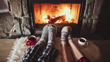 Couple Feet in Woollen Socks by the Cozy Fireplace, 4K. Man and Woman relax by warm fire and warming up their feet. Close up. Winter and Christmas holidays concept. - Powered by Adobe