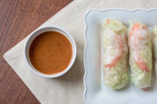 close up sweet creamy peanut sauce and  fresh summer rolls on white plate on wood table