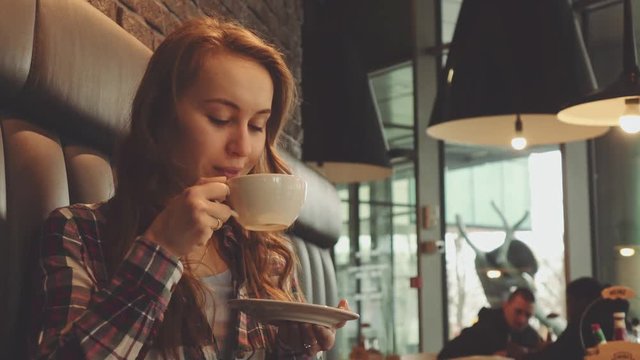 Woman drinking coffee in a cafe, 4K Slow Motion 120 fps. Stabilazed dolly shot. Young beautiful calm woman enjoying a cup of hot coffee in the restaurant. Relaxed morning breakfast in a city. 
