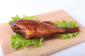 Smoked fish and lemon on green lettuce leaves on Wooden cutting board isolated on white background.
