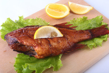 Smoked fish and lemon on green lettuce leaves on Wooden cutting board isolated on white background.