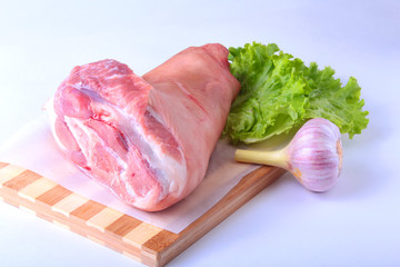 Raw pork knuckle, garlic and lettuce leaves on a cutting board. Selective focus. Ready for cooking.