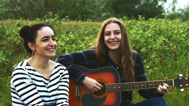 Two beautiful young hipster girls, rejoice and sing to guitar songs. 4K