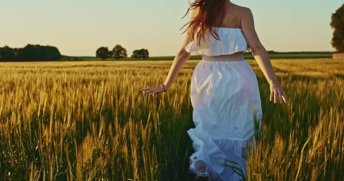 Beautiful girl running on sunlit wheat field. Slow motion 120 fps. Freedom concept. Happy woman having fun outdoors in a wheat field on sunset or sunrise. Slowmo. Harvest.