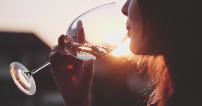 Woman Drinking Cooled White Wine from a glass at the Balcony during Sunset. Slow Motion 120 fps, 4K DCi. Beautiful female enjoying cozy evening on terrace. Summertime relax at sunny patio. Lens Flare