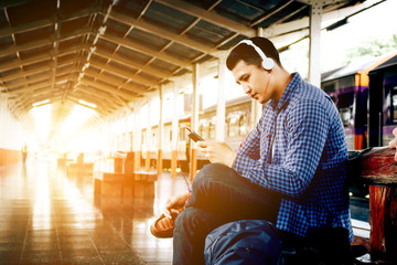 Asian hipster man listening to music at train station with headphones and smartphone.