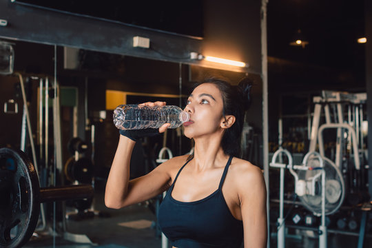 Young asian woman drinking water with refreshing during training at gym.